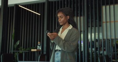 Şık bir ofiste genç bir kadın cep telefonuyla meşgul, modern bir çalışma ortamı sergiliyor..