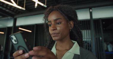 Şık bir ofis ortamında akıllı telefon kullanan genç bir profesyonel odaklanmayı ve konsantrasyonu gösteriyor..