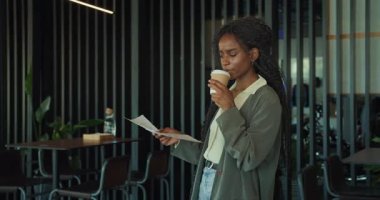 Profesyonel bir kadın şık bir kafe ortamında bir fincan kahvenin tadını çıkarırken önemli evrakları özenle gözden geçirir.