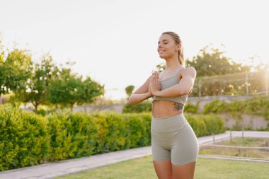 Kendine güvenen bir kadın dışarıda yoga yapıyor, sıcak güneş ışığı ve güzel yeşilliğin tadını çıkarıyor.