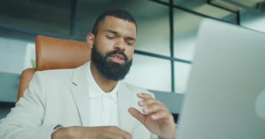 Takım elbiseli bir işadamı, modern bir ofiste dizüstü bilgisayarıyla ciddi bir konuşma yapar.