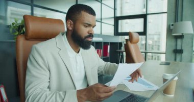 Odaklanmış bir profesyonel, modern bir ofiste verimliliği ve yeniliği destekleyen bir dizüstü bilgisayardaki belgeleri analiz eder.