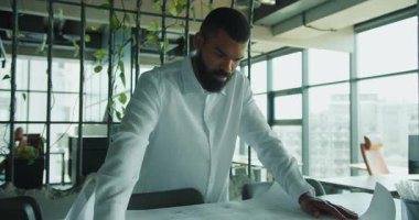 Adanmış ve odaklanmış bir profesyonel modern çalışma ortamında mimari planlarını ayrıntılı bir şekilde gözden geçiriyor.