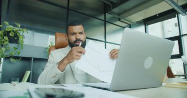 Odaklanmış bir profesyonel, modern bir ofiste üretkenliği ve işbirliğini destekleyen bir dizüstü bilgisayar kullanarak evrakları gözden geçirir.