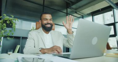 Gülümseyen bir işadamı modern ofisinden sanal bir toplantıda işbirliği ve bağlantıyı destekliyor.