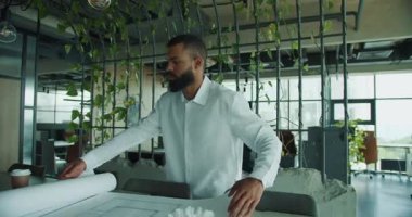 Bir mimar, yaratıcılığa ve yeniliğe ilham veren şık ve bitkisel bir ofiste planları inceler.