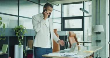 Bir adam, evrak işlerini şık bir ofis ortamında yönetirken aynı anda bir telefon görüşmesi yapıyor.
