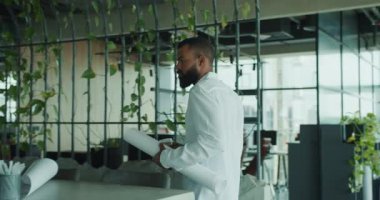 Bir mimar, kendine güveni tam bir planla çevrenin yeşilliklerle dolu canlı ve yemyeşil bir ofisinde duruyor.