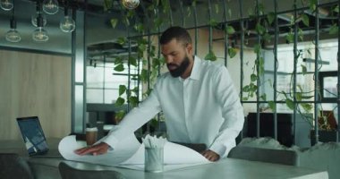 Bir profesyonel, bitkilerle dolu şık bir ofiste mimari planları inceliyor ve işbirliğini vurguluyor.
