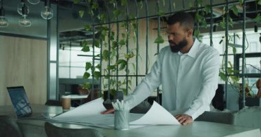 Kendini adamış bir profesyonel, yeşillik dolu çağdaş bir ofiste mimari planları inceliyor..