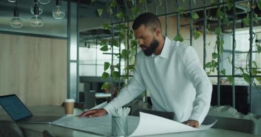 Kendini işine adamış ve odaklanmış bir profesyonel şık bir ofis ortamının ayrıntılı planlarını ayrıntılı bir şekilde inceler.