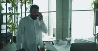 Şık bir adam telefonuyla konuşur modern, bitkisel bir ofiste otururken parlak doğal ışıkla.