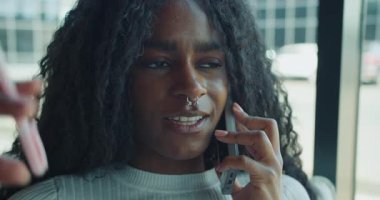Kıvırcık saçlı genç bir kadın, canlı bir ortamda bir dizi duyguyu ifade eden bir telefon konuşmasında yer alıyor.