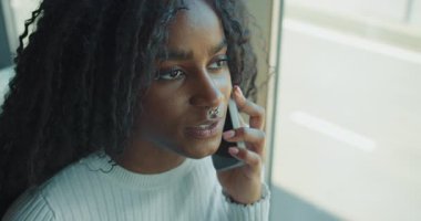 Genç bir kadın, pencerenin önünde otururken düşünceli ve odaklanmış bir ifade sergiliyor.