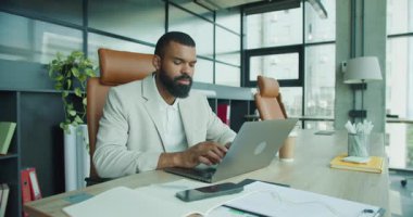 Kendini işine adamış ve profesyonel bir adam modern ve şık bir ofis alanında dizüstü bilgisayarı üzerinde çalışıyor.