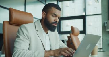 Modern ve şık bir ofis ortamında, özel dikim takım elbiseli kararlı bir adam özenle MacBook 'unu yazar.