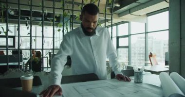 Bir mimar şık bir ofis ortamında karmaşık ve ayrıntılı inşaat planlarını dikkatlice inceler.