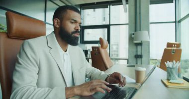 Odaklanmış bir profesyonel, çağdaş ofis ortamında dizüstü bilgisayar üzerinde çalışırken belgeleri değerlendirir..