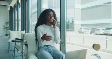 Genç bir kadın, modern bir ofis ortamında otururken telefonla güvenli bir şekilde konuşuyor.