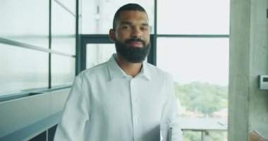 Gıcır gıcır beyaz gömlekli kendine güvenen bir adam bilgisayarını kullanarak parlak ve modern bir ofiste ustaca geziniyor.