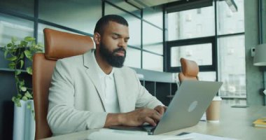 Kendini işine adamış ve yetenekli bir profesyonel stil ve modern ofis ortamında özenle bir dizüstü bilgisayar üzerinde çalışıyor.