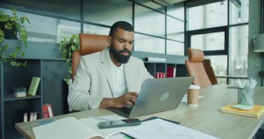 Kendini işine adamış bir işadamı, yaratıcılık ve üretkenlik için tasarlanmış modern bir ofiste dizüstü bilgisayarı üzerinde çalışıyor.