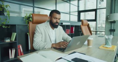 Odaklanmış bir birey, modern bir ofiste dizüstü bilgisayarla çalışıyor. Yüksek verimliliği açıkça gösteriyor.