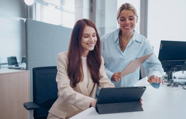 Modern bir ofis ortamında, iki yetenekli profesyonel bir tablet kullanarak iletişim kurar ve işbirliği yaparlar.