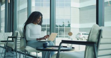 Kararlı genç bir kadın laptopunu yoğun bir şekilde modern bir kafede kullanıyor.