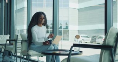 Genç bir kadın, modern bir kafede laptopuyla çalışırken kahvenin keyfini çıkartıyor.