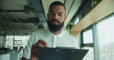 Kendini işine adamış bir profesyonel şık bir ofiste, üretkenliği artıran doğal ışıkla bir panoyu inceliyor.