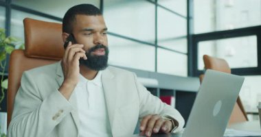 Çalışkan bir iş adamı, önemli bir telefon üzerine modern bir ofiste laptopunu etkin bir şekilde kullanır.