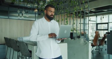 Kendini işine adamış ve işine odaklanmış bir adam şık bir ofis ortamında laptopuyla çalışıyor. Etrafı yemyeşil.