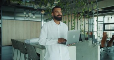 Modern bir ofiste oturan bir adam, dizüstü bilgisayarıyla meşgul, çağdaş çalışma kültürü ve yaratıcılığını somutlaştırıyor.