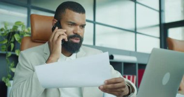 Modern ofis ortamında önemli bir çağrı sırasında önemli belgeleri özenle analiz eden bir iş adamı