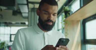 İşadamı, şık ve açık bir çalışma alanında bulunduğu sürece mobil cihazına derinden odaklanmış durumda.