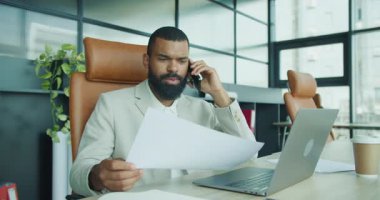 Bir telefon görüşmesi için uygun bir profesyonel masasındaki önemli belgeleri gözden geçirir, kendini adamışlık ve verimliliği gösterir.