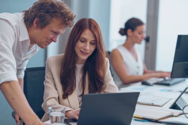 Modern ofis ortamında dizüstü bilgisayarda birlikte çalışan iki yetenekli profesyonel.