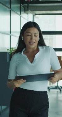 Modern ofis ortamında bir kadın yürürken, profesyonel tavrını sergilerken bir tablet kullanır..