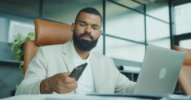 Şık bir ofiste profesyonel bir adam, telefon ve dizüstü bilgisayarla iletişim kuruyor, iş zekasını sergiliyor..