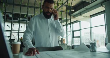 İşadamı, şık bir çalışma alanındaki mimari planları analiz ederken bir telefon görüşmesi yaptı..
