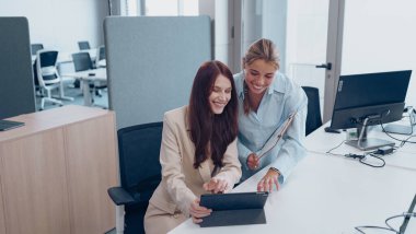 İki profesyonel kadın modern bir çalışma alanında iş birliği yaparken aktif olarak bir tabletle uğraşıyorlar.