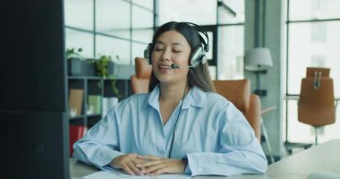 Kulaklıkla donatılmış odaklanmış bir kadın, modern bir çalışma alanı ortamında bilgisayarına derinden bağlıdır. Yüksek kalite 4k görüntü