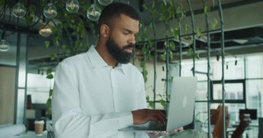 Çalışkan bir adam, modern çağdaş ofis alanındaki bilgisayarına yoğunlaşmıştı. Yeşillik doluydu.