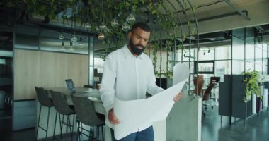 Odaklanmış bir adam şık bir ofisin planlarını inceler. İlham için canlı yeşillikle zenginleştirilir.