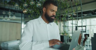 Kendini işine adamış bir adam, üretkenlik ve yaratıcılık için tasarlanmış modern, bitkisel bir çalışma alanında dizüstü bilgisayarıyla çalışır.