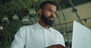 Canlı bitkilerle dolu iyi tasarlanmış, şık bir ofiste profesyonel bir adam yoğun bir şekilde dizüstü bilgisayarına odaklanır.