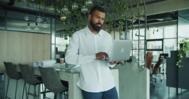 Kendini işine adamış bir profesyonel, yeşilliklerle dolu şık ve modern bir ofis alanında özenle bir dizüstü bilgisayar üzerinde çalışıyor.