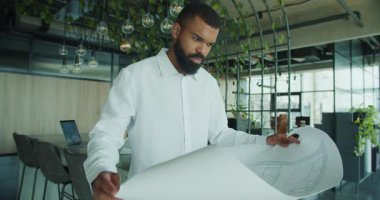 Bir mimar, modern bir ofiste yaratıcı ve yenilikçi bir tasarım sergileyen karmaşık planlara odaklanır.