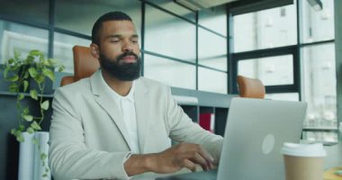 Kendini işine adamış, takım elbiseli, modern ofis ortamında özenle dizüstü bilgisayarıyla çalışan bir adam.